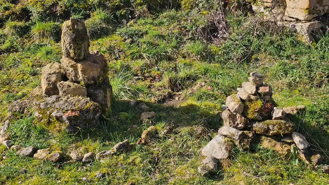 Deux cairns de pierres sèches dans l’herbe, au soleil.