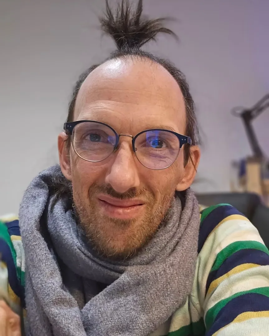 Carlos Chapman, écharpe grise et pull rayé, sourit à l’objectif.